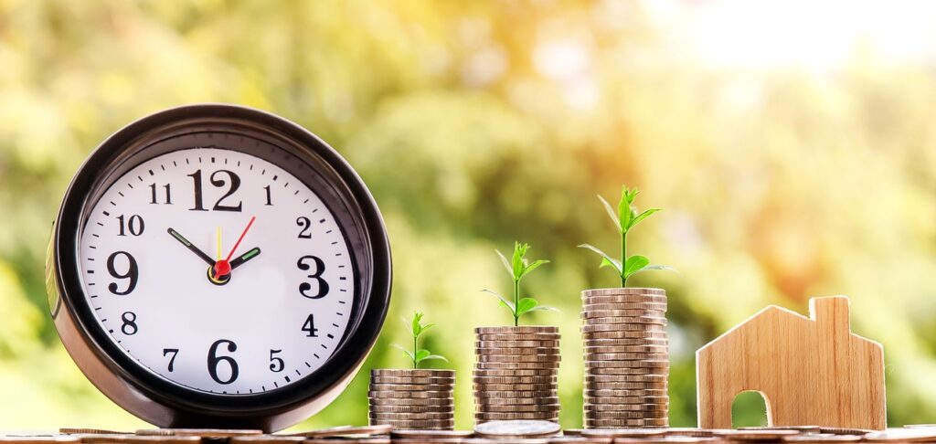 Growing stack of coins with trees, house, and clock representing financial growth and stability."